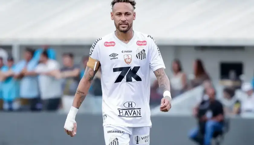 Neymar w białej koszulce Santos, z opaską na ramieniu, na boisku. To właśnie tam gra Neymar, kiedyś gwiazda tego klubu.