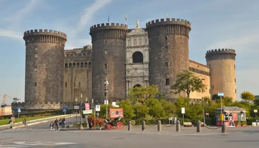 Castel Nuovo w Neapolu, imponująca forteca z wieżami i bramą, to jedno z miejsc, które warto zobaczyć. Obok przejeżdża dorożka.