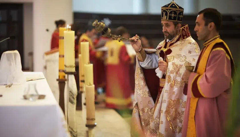 Dwaj duchowni w szatach liturgicznych podczas nabożeństwa, jeden z kadzielnicą, obok świece.