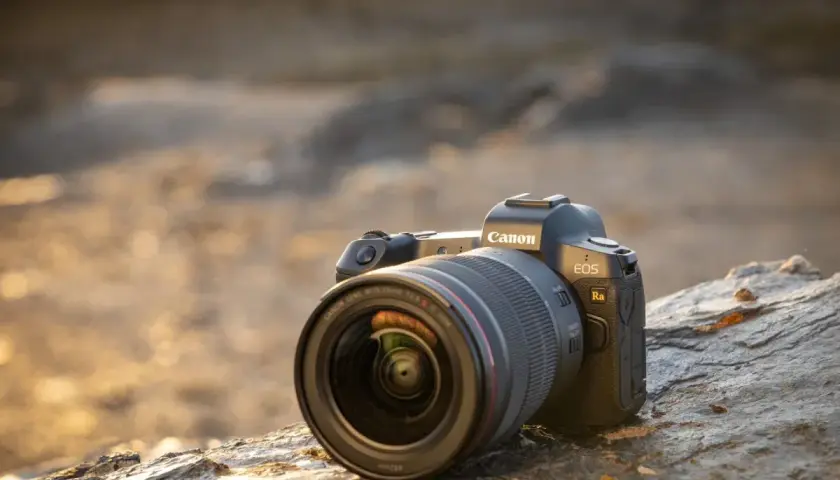 Profesjonalny aparat do astrofotografii Canon EOS Ra z obiektywem RF 15-35mm f/2.8 L IS USM leży na kamieniu.