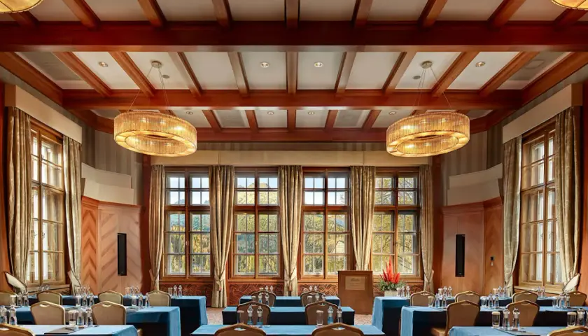 Elegancka sala konferencyjna w Kempinski Hotel, z drewnianymi belkami na suficie, dużymi oknami z widokiem na jesienny krajobraz i stylowymi żyrandolami.