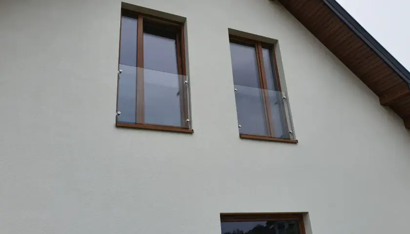 Nowoczesny portfenetr z drewnianymi ramami i szklaną balustradą na białej elewacji.
