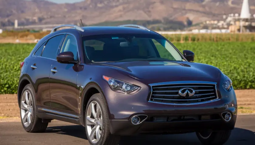 Elegancki, ciemnobordowy Infiniti QX70 stoi na tle krajobrazu z polami i górami.