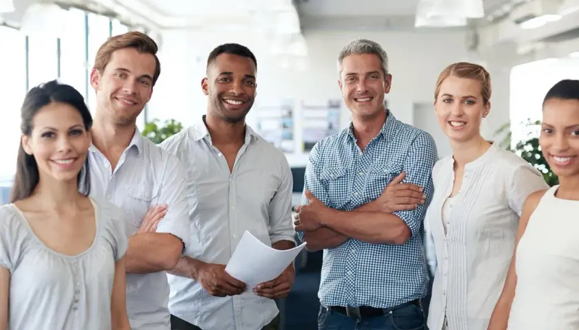 A diverse team smiles confidently, showcasing what employee engagement looks like. They stand together in a bright office, radiating positivity and collaboration.