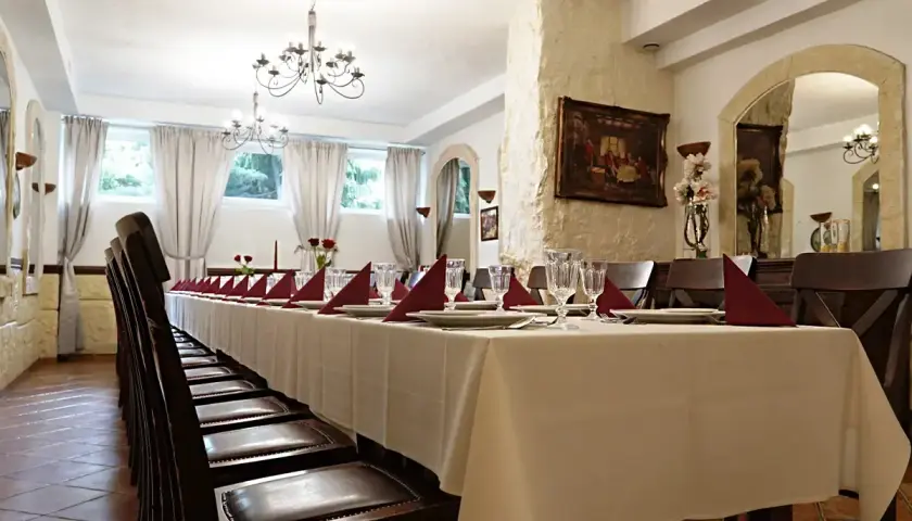 Długi stół w restauracji, nakryty białym obrusem, z czerwonymi serwetkami i kieliszkami. Czy rezerwacja stolika w restauracji jest płatna?