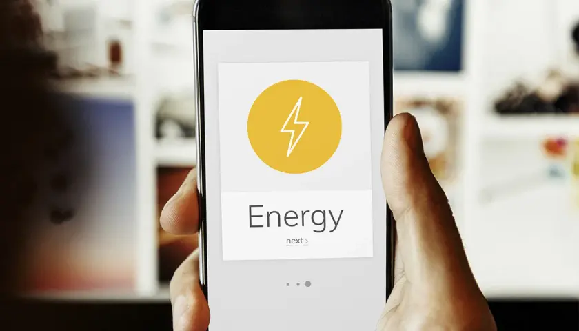 Mano sujetando un smartphone con una app de monitorización energética. El icono de un rayo y la palabra "Energy" indican el control del consumo.