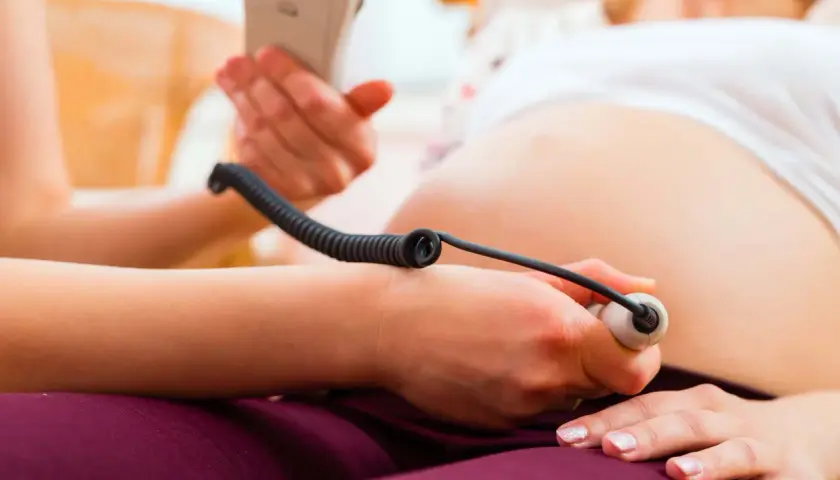 En barnmorska lyssnar på ett barns hjärtljud med en doppler. En del av en gravid mage syns. Inskrivning gravid.