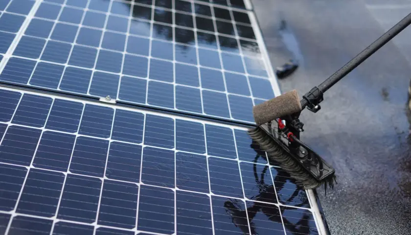 Brosse rotative en action pour nettoyer panneau solaire. L'eau ruisselle sur les cellules bleues et brillantes.