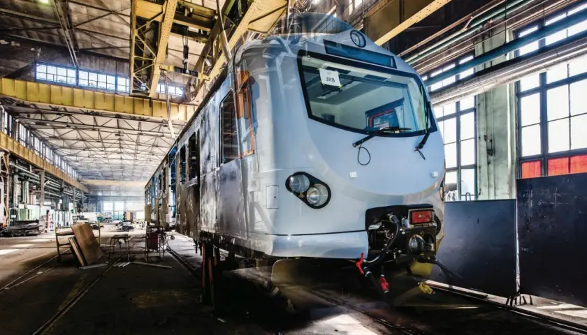 Nowy pociąg EN57 przechodzi modernizację w hali produkcyjnej. Widać jego front i część wagonu.