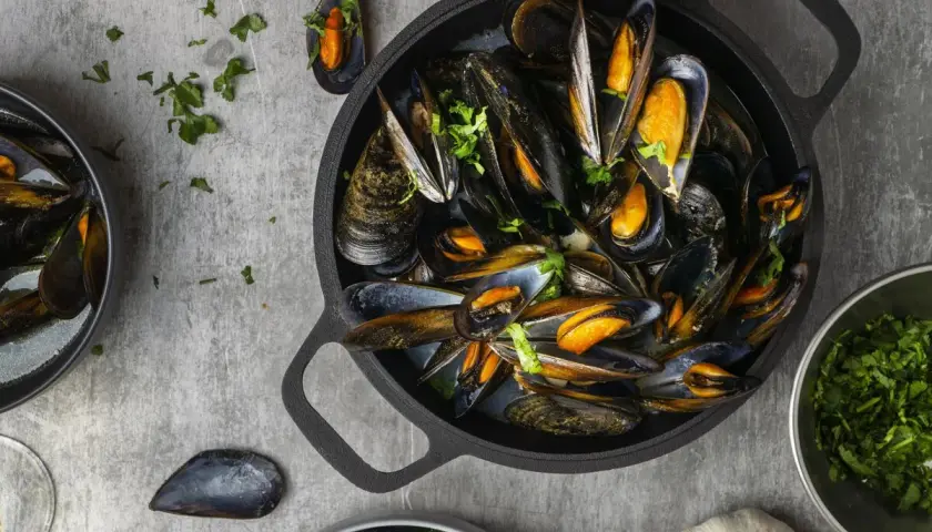 Una deliciosa preparación de mejillones, mostrando que son los mejillones, servidos en una sartén negra con perejil fresco y limón.