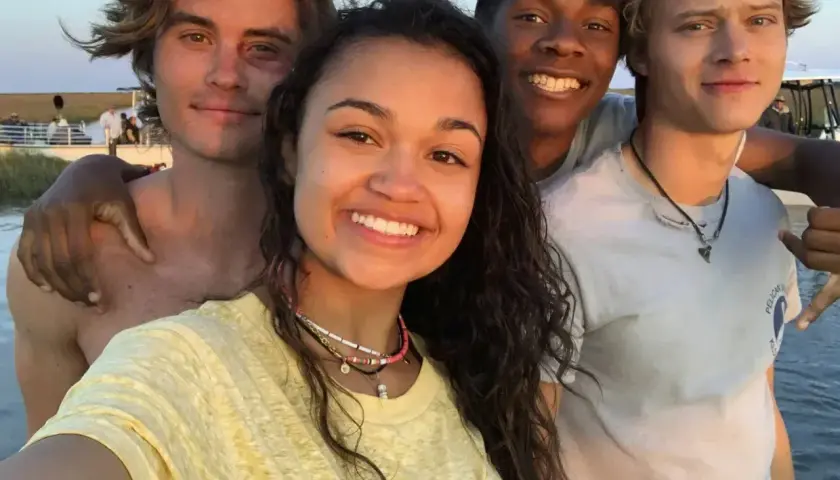 Uśmiechnięta **outer banks obsada** pozuje do selfie na plaży.