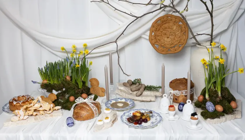 Wielkanocna oferta cateringowa: stół z tradycyjnymi potrawami, babkami, chlebem, jajkami i wiosennymi kwiatami.