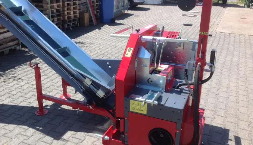 Rote Maschine mit einem langen, schrägen Förderband, bereit für den Einsatz. Diese Kreissäge mit Förderband ist ein robustes Gerät für die Holzverarbeitung.