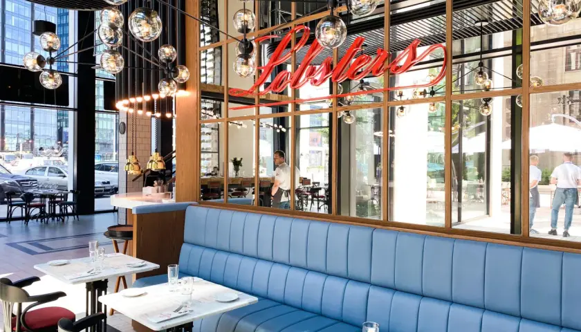 Elegancka restauracja z owocami morza w Warszawie. Neonowy napis "Lobster" nad błękitnymi kanapami.