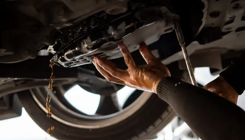 Mechanik spuszcza olej z miski olejowej. Dowiedz się, ile kosztuje wymiana oleju u mechanika.