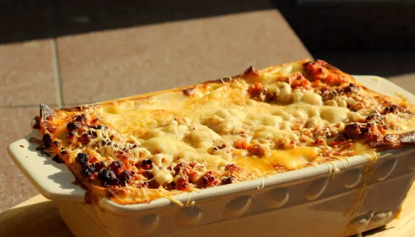 Gorąca, zapieczona lasagne orzepis w naczyniu, z ciągnącym się serem i rumianymi brzegami.