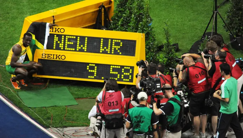 Usain Bolt, najszybszy człowiek świata, świętuje nowy rekord świata 9.58s. Otoczony przez fotoreporterów, z flagą Jamajki.