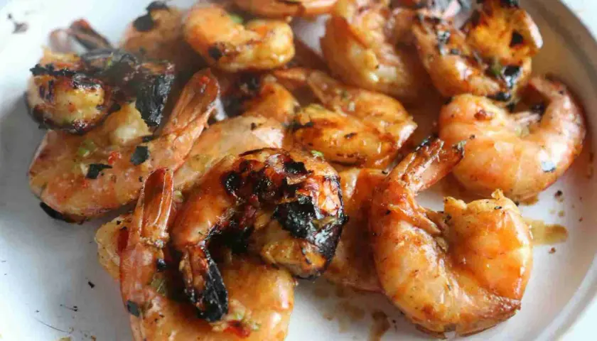 Grosses crevettes bbq, grillées à la perfection, avec des marques de cuisson foncées et une sauce savoureuse.