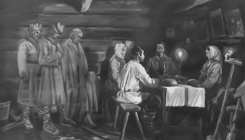 Ludzie w tradycyjnych strojach, w tym dzieci, zebrani w izbie. Na stole świeca, obok narzędzia. Atmosfera przypomina obrzędy dziadów.