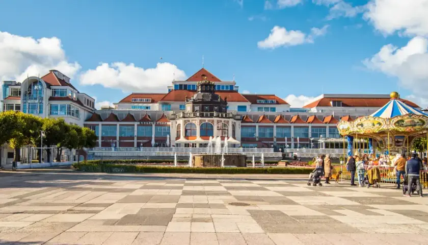 Sopot, część Trójmiasta, co to za miejsce? Plac z karuzelą i fontanną przed pięknym budynkiem.