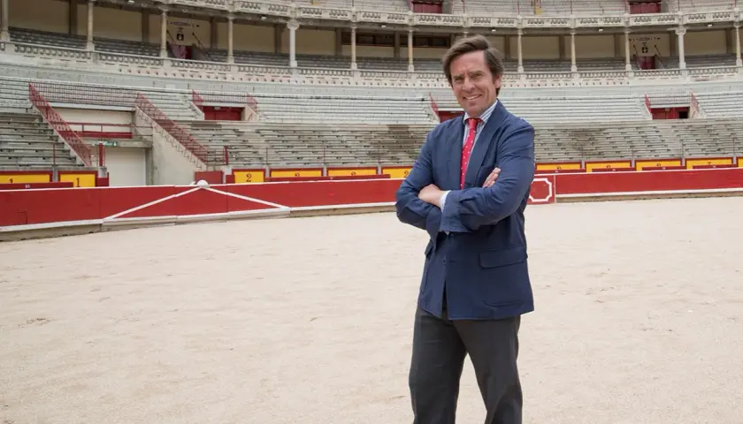 Eduardo Dávila Miura, con traje azul y corbata roja, posa en el ruedo de una plaza de toros.