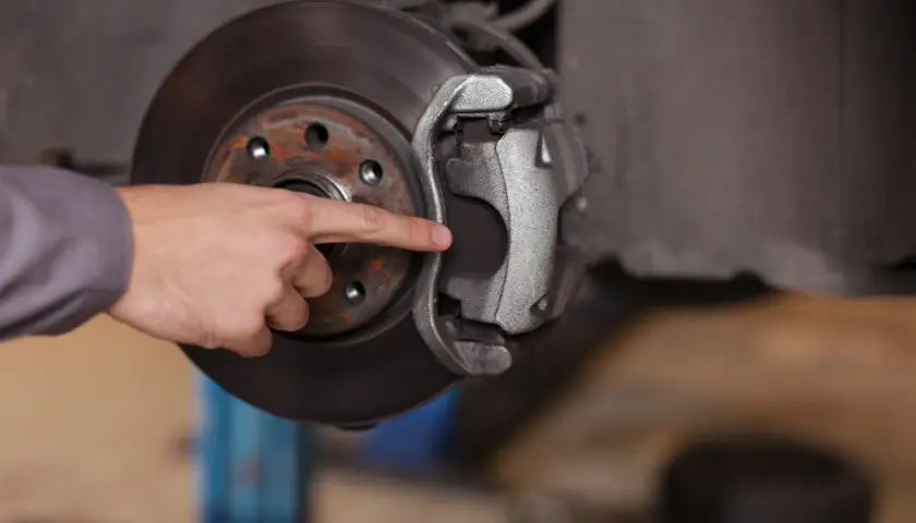 A mechanic's finger points to the dot brake pad thickness, indicating it's time for a replacement.