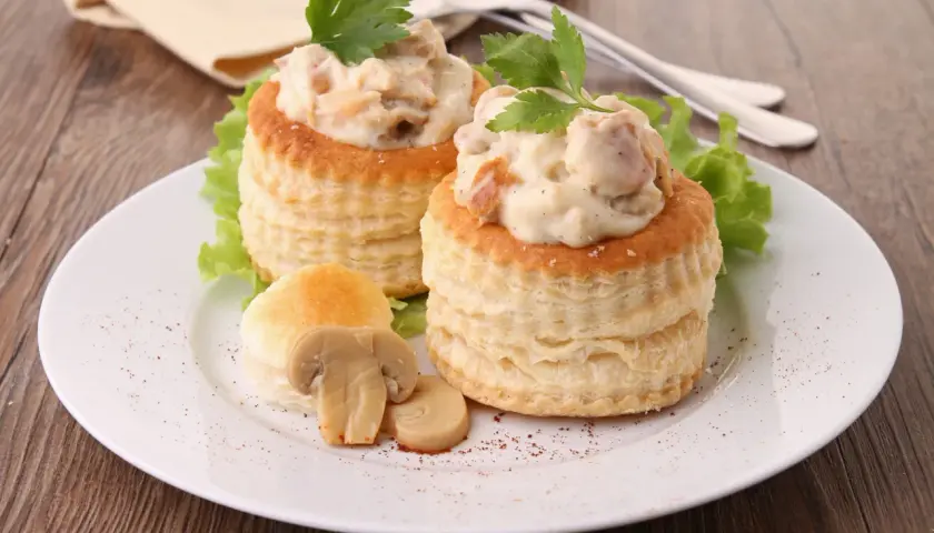 Deux vol-au-vent poulet crémeux, garnis d'une sauce onctueuse et de morceaux de poulet, décorés de persil frais et accompagnés de champignons.
