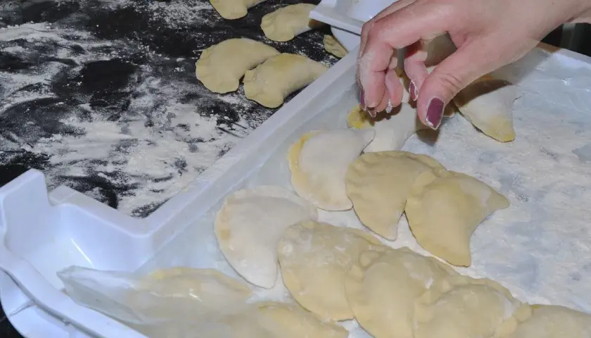 Ręka układa pierogi na tacy, posypanej mąką. Aby ugotowane pierogi się nie skleiły, warto je od razu po ugotowaniu delikatnie polać tłuszczem.