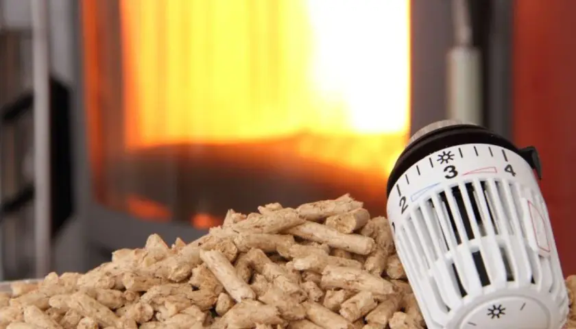 Holzpellets vor einem Kaminfeuer, daneben ein Thermostat zur CO2-Steuer.