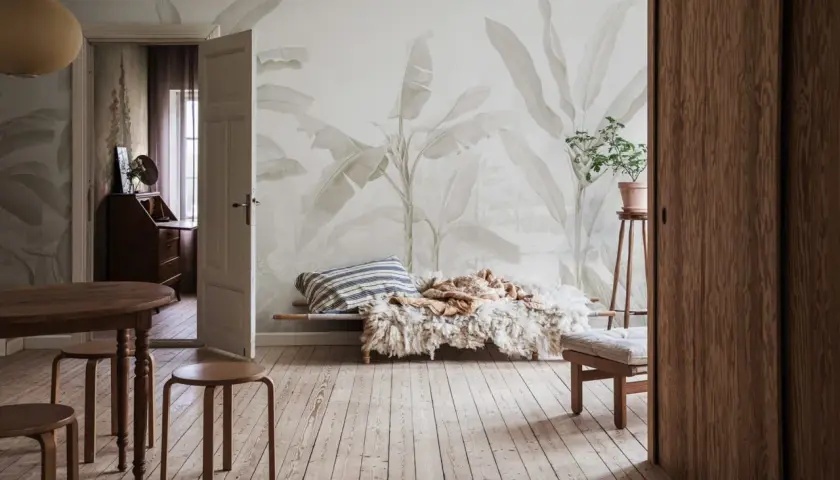 Salon w stylu boho z tapetą w liście bananowca, drewnianymi meblami i przytulnym legowiskiem.