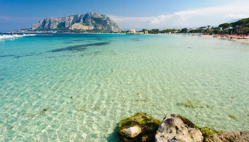 Acque cristalline e un promontorio maestoso fanno da sfondo a una giornata di sole al mare a Palermo.
