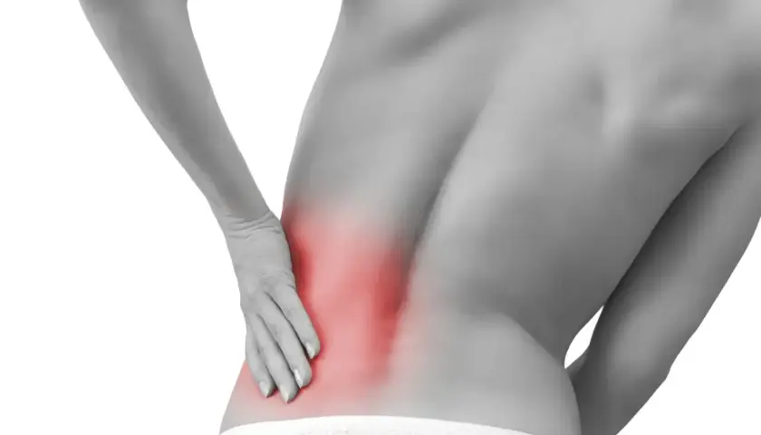 Persona con dolor en la espalda baja, señalando una zona roja que indica contractura lumbar.