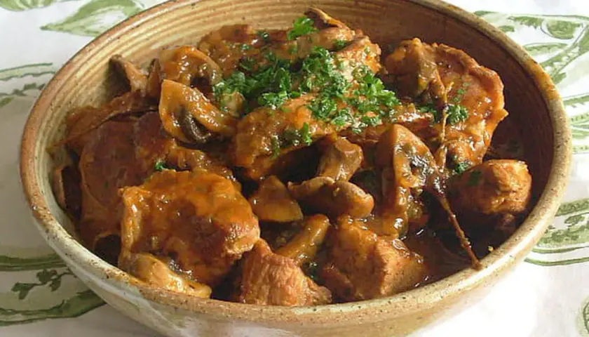 Un délicieux sauté de veau aux champignons, garni de persil frais, servi dans un bol en terre cuite.