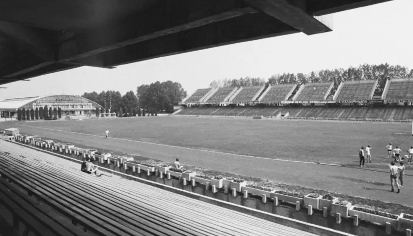 Widok na stary stadion Stali Mielec z pustymi trybunami i boiskiem, gdzie trenuje kilku piłkarzy.