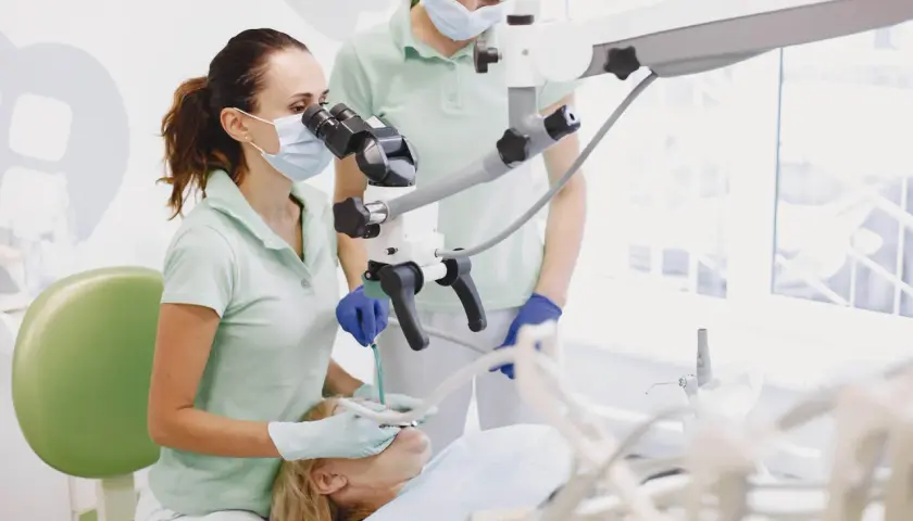 Dentystka z asystentką używają mikroskopu stomatologicznego, by skutecznie leczyć ból ósemki.