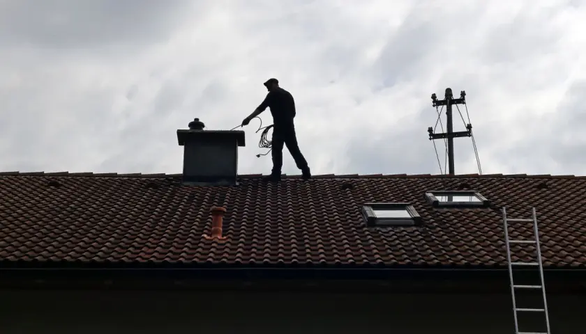 Kominiarz na dachu czyści komin. Zastanawiasz się, ile kosztuje pozwolenie na budowę komina?