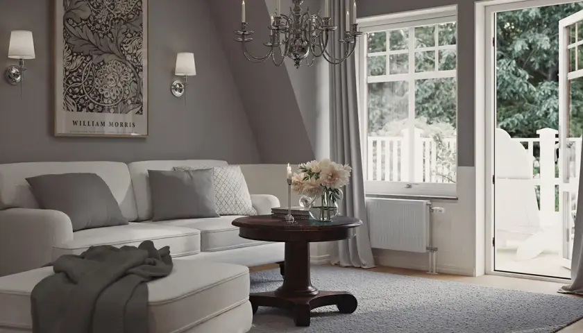 En ljus och luftig salong med sekelskifte inredning. En vit soffa med kuddar, ett runt träbord med blommor och en öppen balkongdörr.