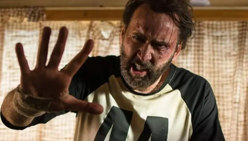 Nicolas Cage med blåmärken och svettig panna, höjer handen i en gest av stopp. En scen från en av hans filmer.