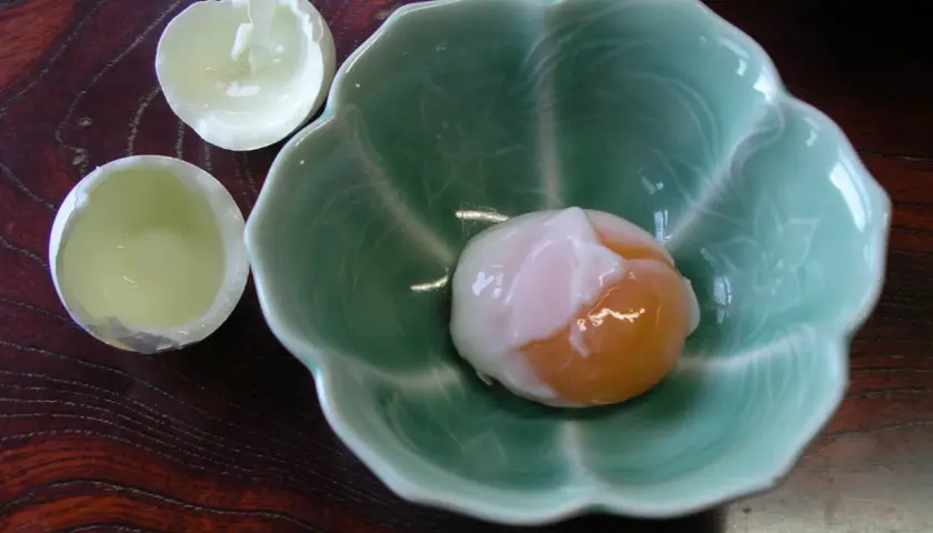 A perfectly soft-boiled egg, a delicacy of Japanese eggs, rests in a green, petal-shaped bowl.