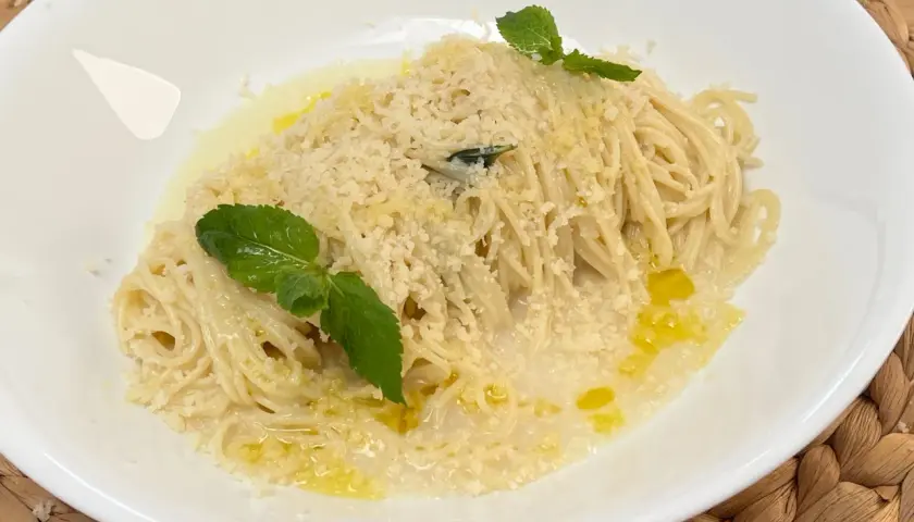 Spaghetti al limone cremosi, conditi con parmigiano grattugiato, olio d'oliva e guarniti con foglie di menta fresca.