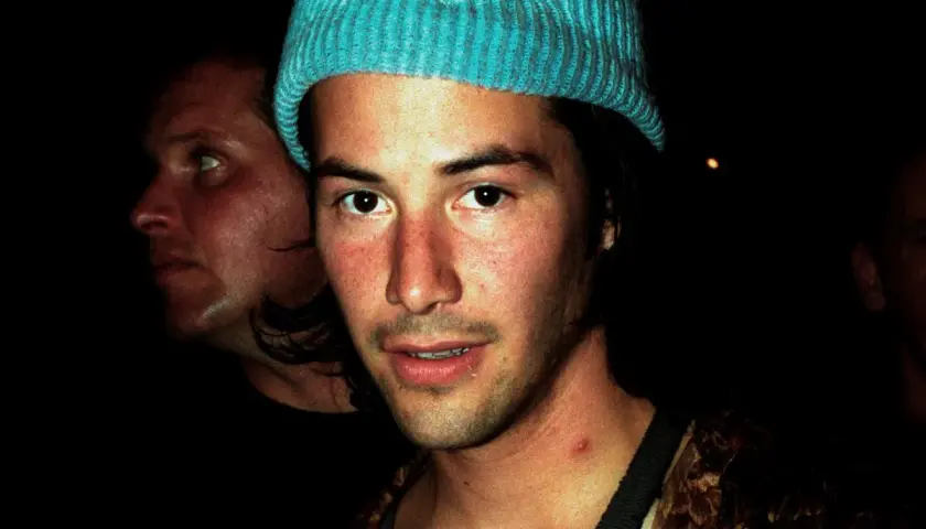 Młody Keanu Reeves w niebieskiej czapce, obok niego inny mężczyzna. Trudno zgadnąć, ile lat ma Keanu Reeves na tym zdjęciu.