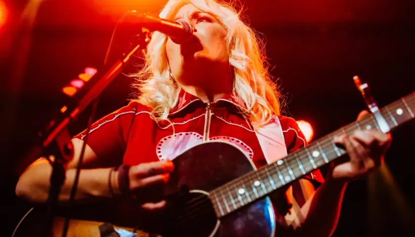 Maja Francis sjunger och spelar gitarr på en scen, upplyst av rött ljus.