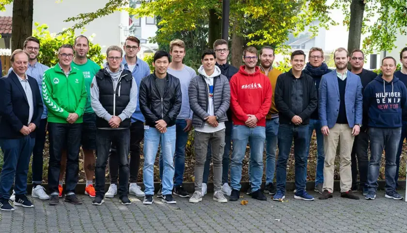 Eine Gruppe junger Männer steht lächelnd im Freien. Vielleicht sind sie angehende Fußball-Scouts, die ihre Ausbildung beginnen.