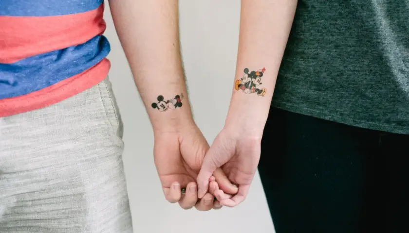 Para trzymająca się za ręce, z tatuażami Myszki Miki na nadgarstkach. Tatuaż myszka miki znaczenie - symbolizuje wieczną przyjaźń i dziecięcą radość.