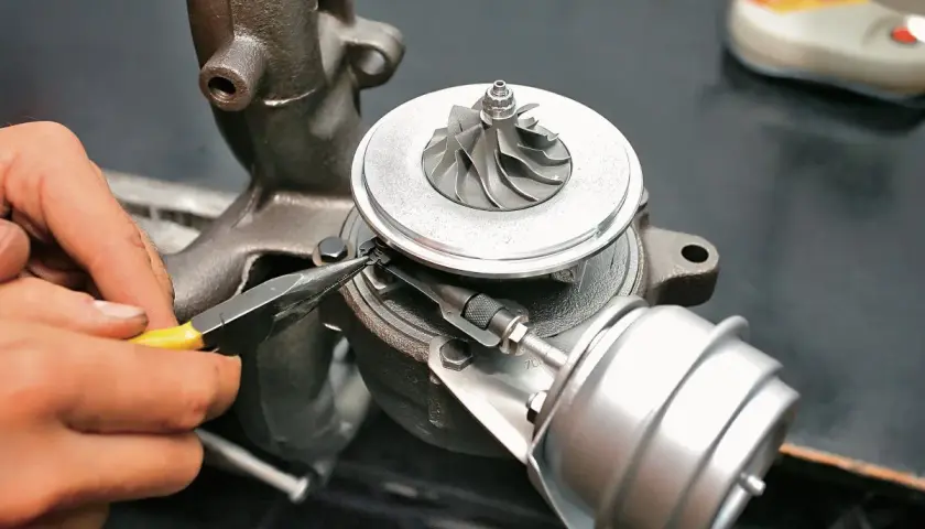 Mechanik precyzyjnie pracuje nad nastawnikiem turbiny, używając szczypiec. Trwa regeneracja turbosprężarki.