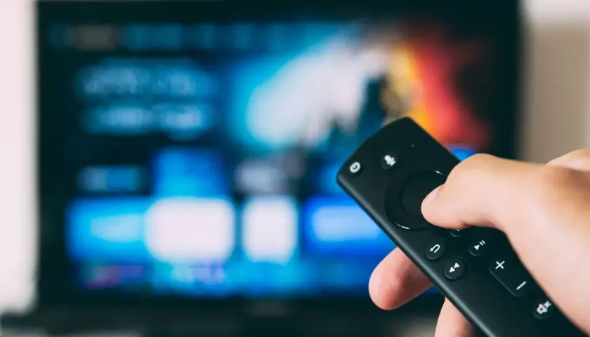 Fernsehen ohne Anschluss und ohne Internet: Eine Hand hält eine Fernbedienung vor einem unscharfen Bildschirm mit bunten Menüs.