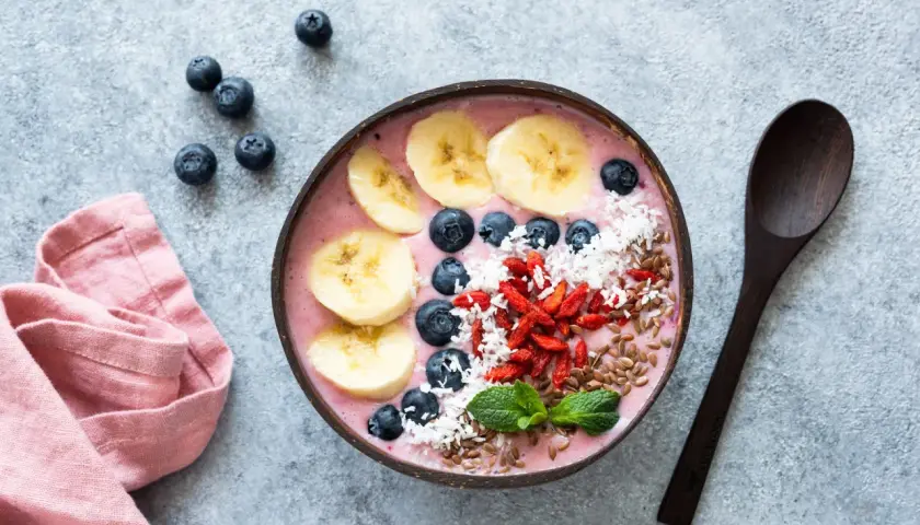 Kolorowa bowl z owocami: banan, borówki, jagody goji, wiórki kokosowe i siemię lniane. Idealna na zdrowe śniadanie, inspiracja z bowl przepisy.