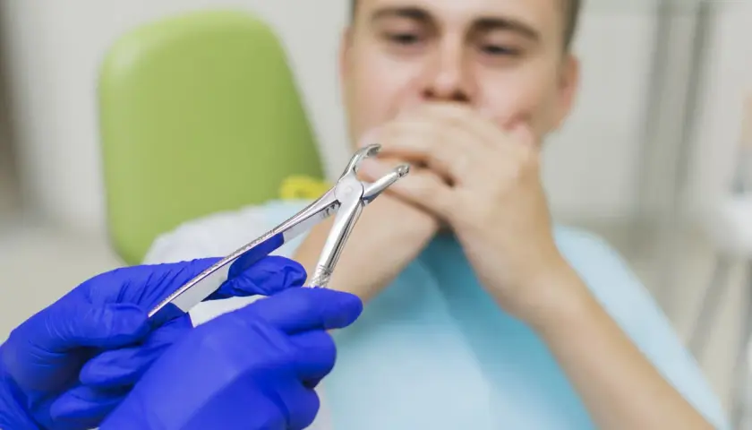 Dentysta w niebieskich rękawiczkach trzyma kleszcze, pacjent zasłania usta. Czy 8 trzeba wyrwac?