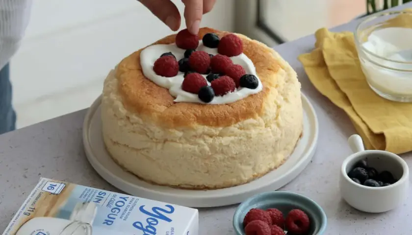Deliciosa tarta de yogur griego esponjosa, decorada con frambuesas y arándanos frescos.