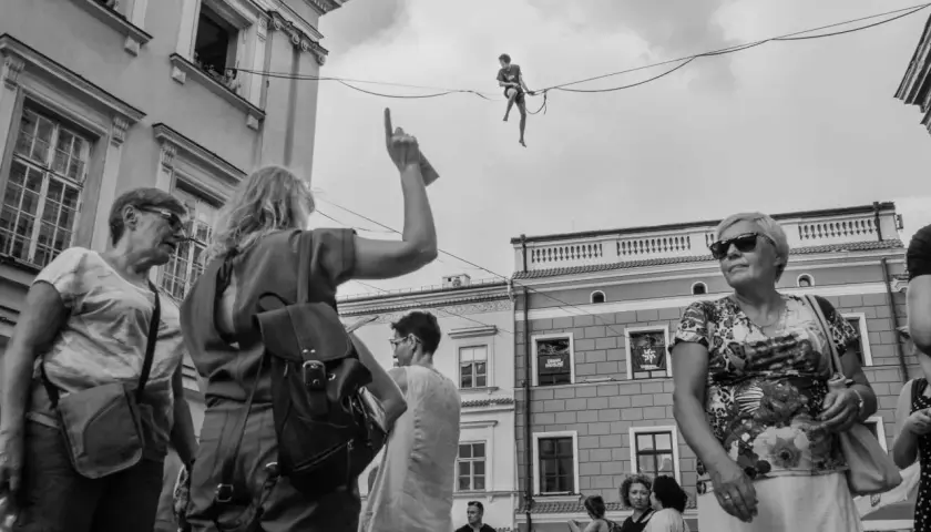 Uliczna fotografia: człowiek balansuje na linie, tłum obserwuje z dołu.